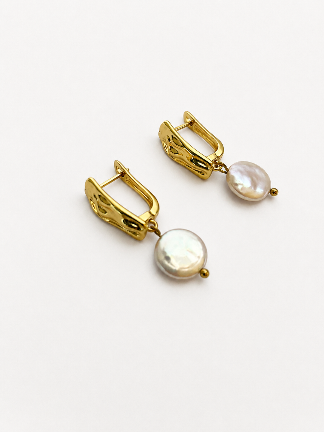Angled view of gold rectangle drop earrings with flat white freshwater coin pearl pendants