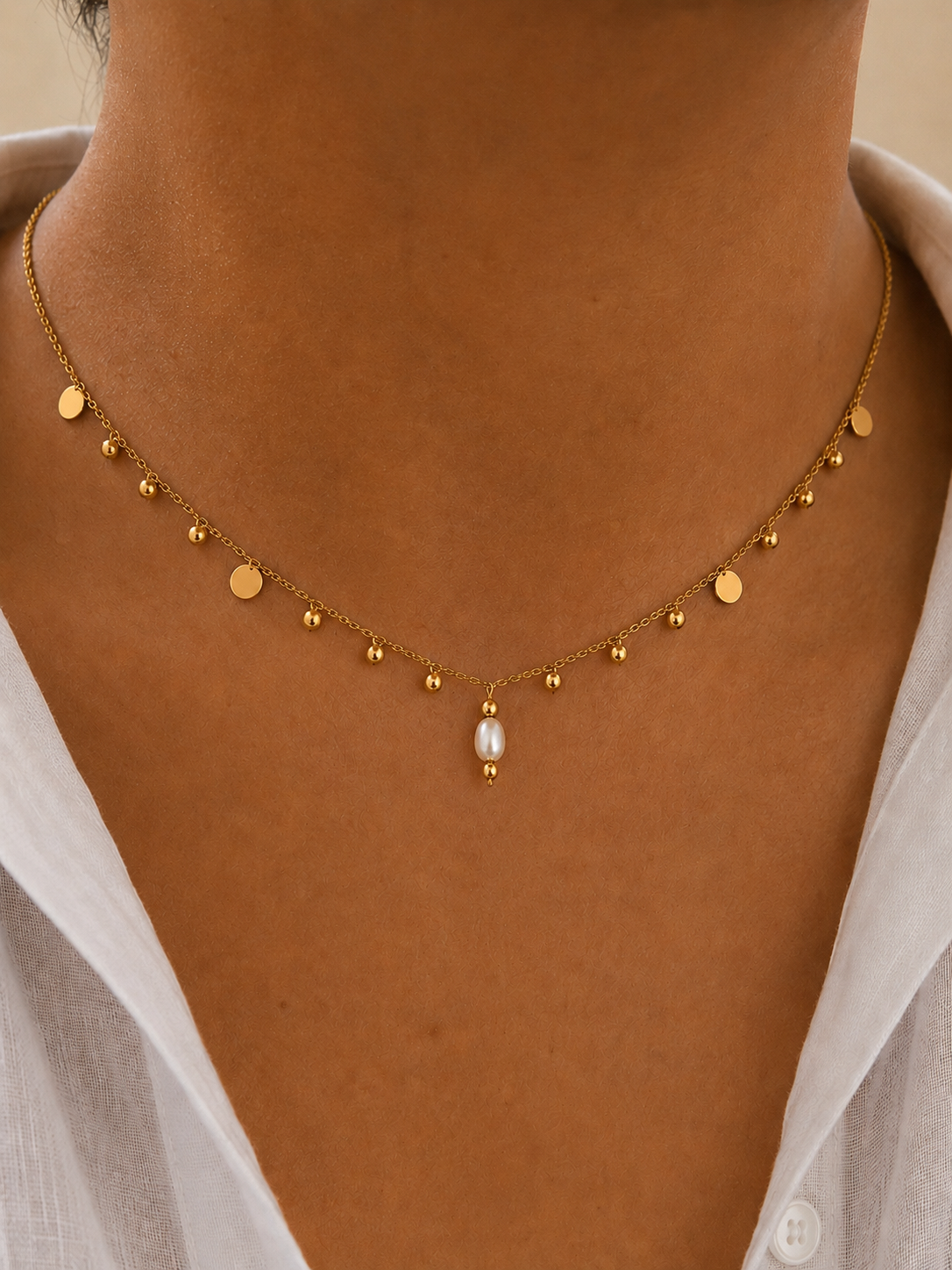 Close-up of a gold bead charms necklace with a 6 mm oval white freshwater pearl worn on the neck