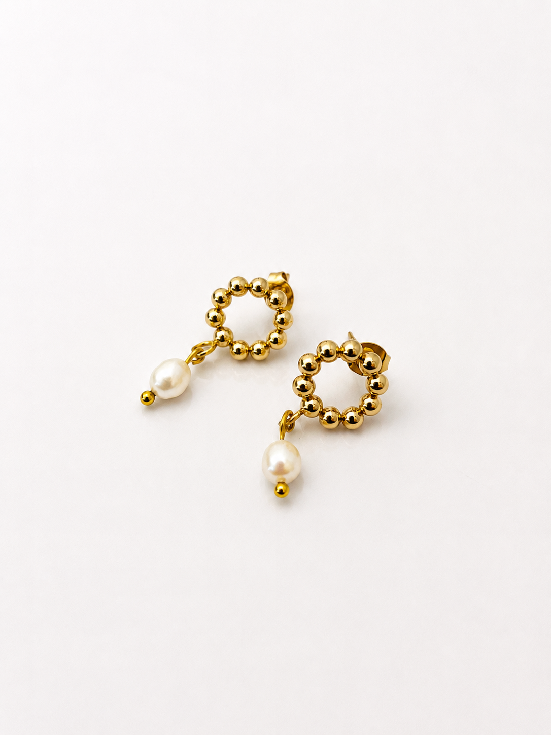 Angled view of beaded gold circle stud earrings with white freshwater pearl drops.