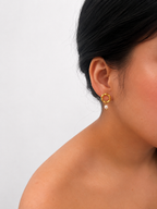 Woman wearing a textured gold circle drop earring with an oval white freshwater pearl.