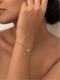 Woman wearing a gold double-chain bracelet with a petite white freshwater pearl pendant and polished gold beads