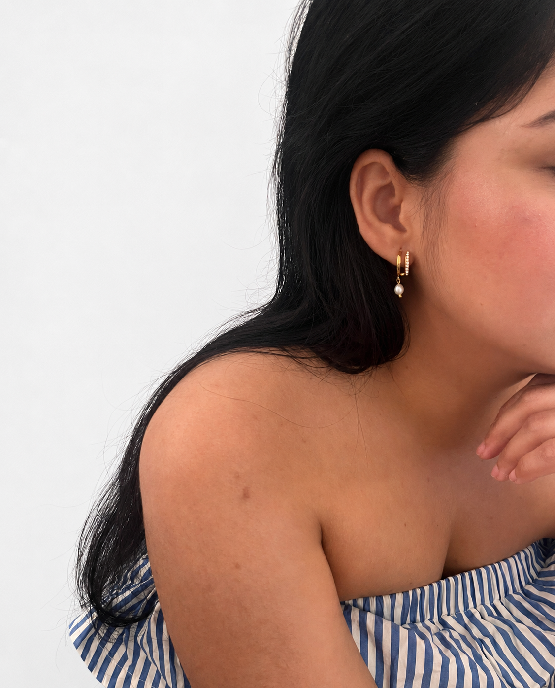 Woman wearing a gold half moon huggie earring with a 6 mm oval white freshwater pearl drop