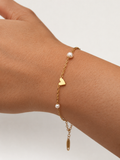 Close-up of a gold chain bracelet with white freshwater pearls and a polished heart charm on the wrist
