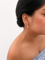 Woman wearing a gold mini drop earring with a white freshwater pearl and cubic zirconia accents.