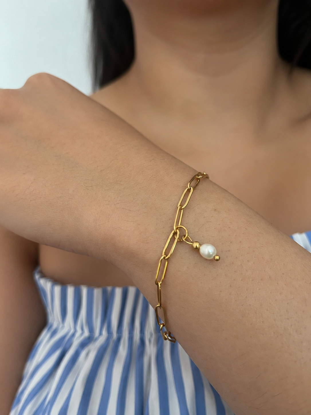 Close-up of a gold paperclip-chain bracelet with an oval white freshwater pearl drop on the wrist