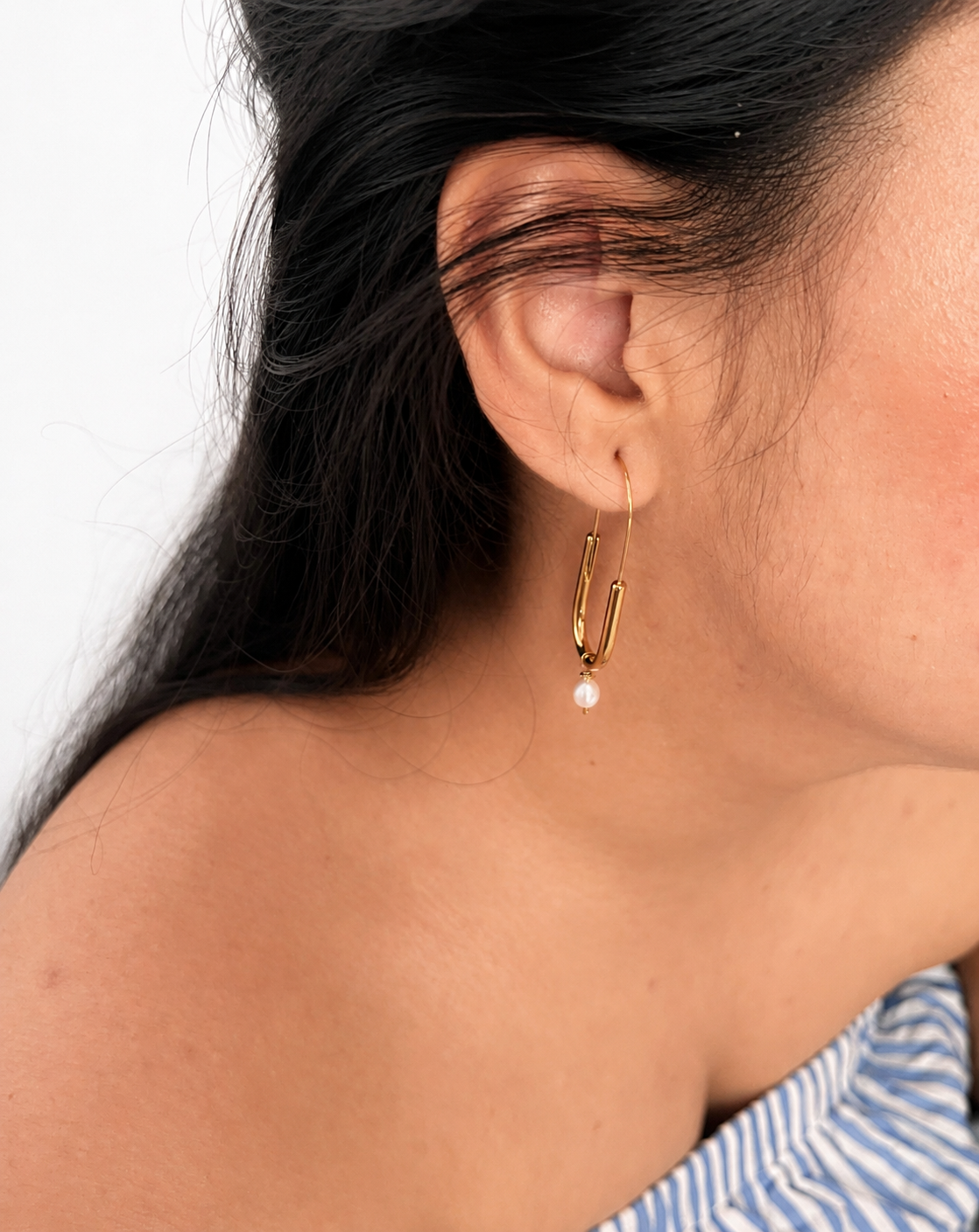 Woman wearing a gold paperclip drop earring with a 5 mm white freshwater pearl pendant