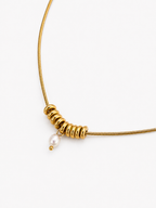 Close-up of a gold Ripple necklace with sculptural ring details and an oval white freshwater pearl pendant