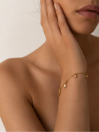 Woman wearing a delicate gold bracelet with a white freshwater pearl and clear stone accents