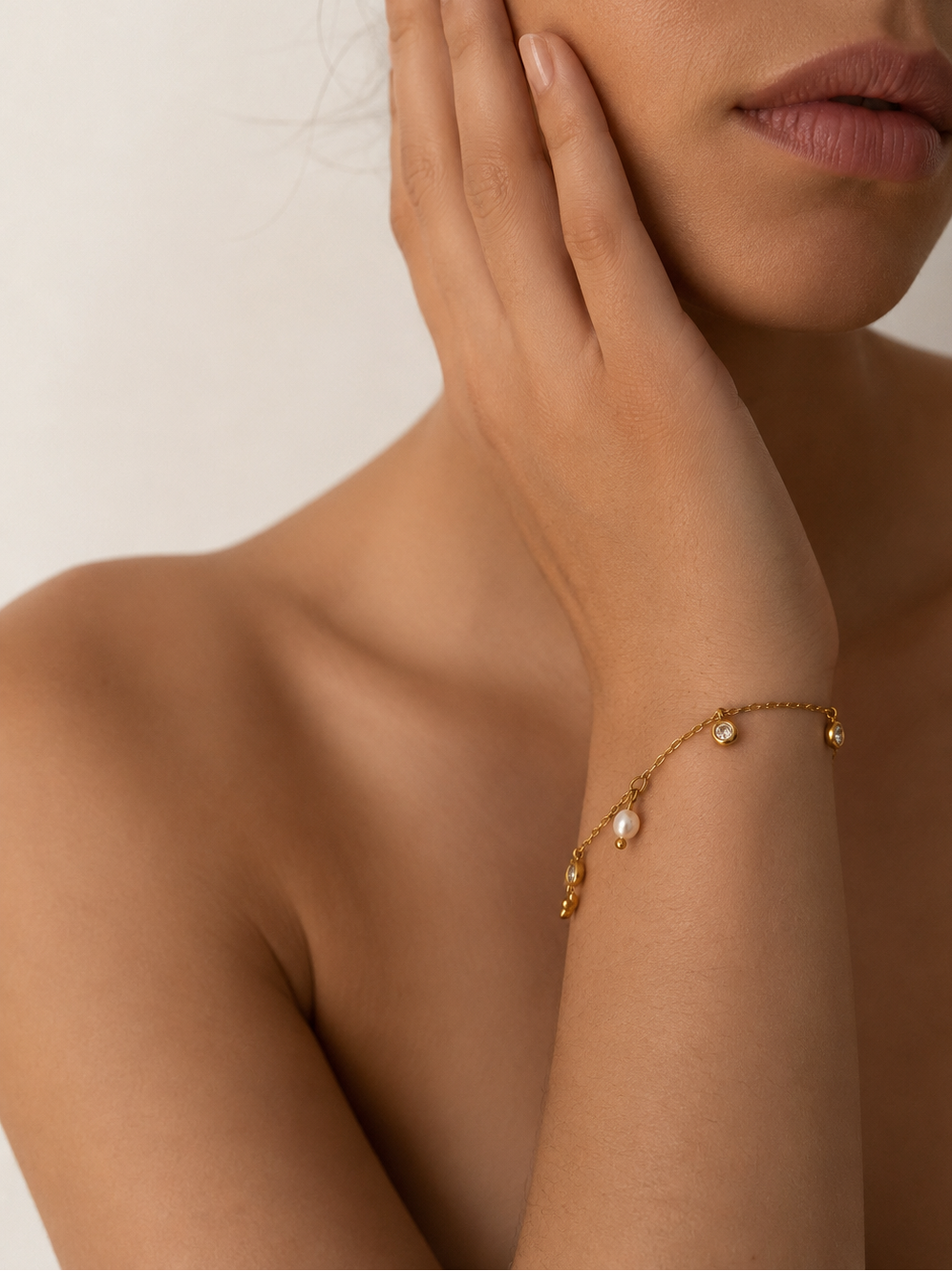Woman wearing a delicate gold bracelet with a white freshwater pearl and clear stone accents