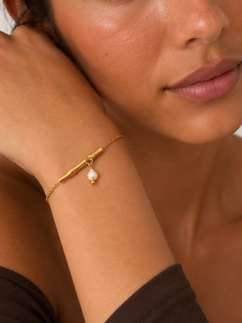 Close portrait of a woman wearing a gold twig bracelet with a white freshwater pearl drop