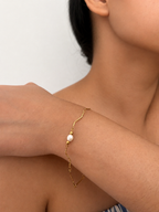 Woman wearing a gold wave-chain bracelet with an oval white freshwater pearl and polished gold beads