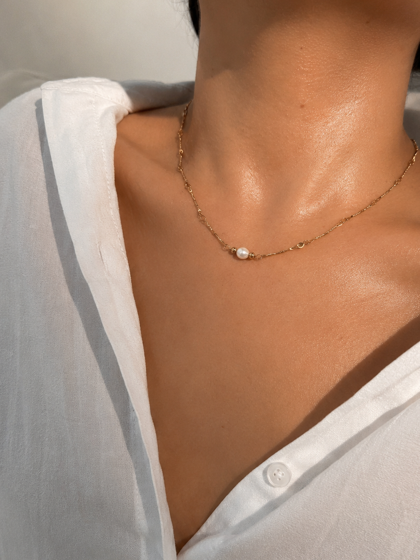 Woman wearing a gold Waves necklace with a 6 mm oval white freshwater pearl.