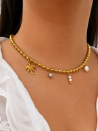 Close-up of a gold beaded necklace with 10 mm white Keshi and 6 mm grey freshwater pearl charms worn on the neck