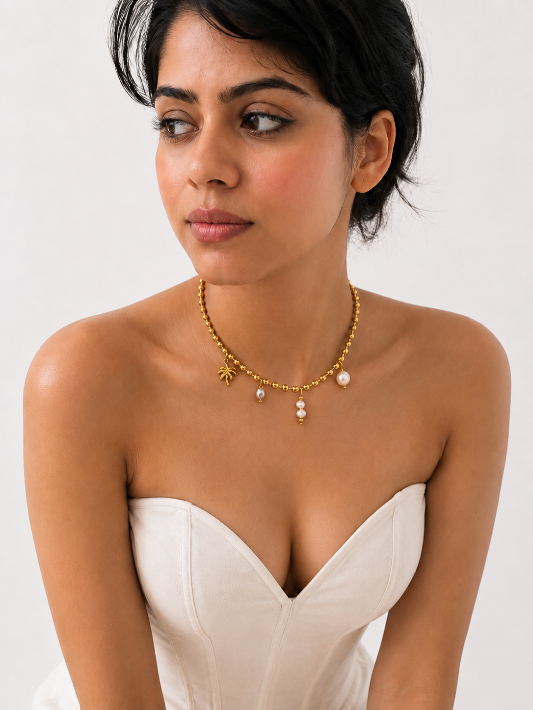 Woman wearing a gold beaded charm necklace with white Keshi pearls, a grey freshwater pearl and palm tree charm