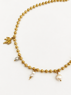 Close-up of a gold beaded charm necklace with white Keshi pearls, a grey oval freshwater pearl and palm tree charm.