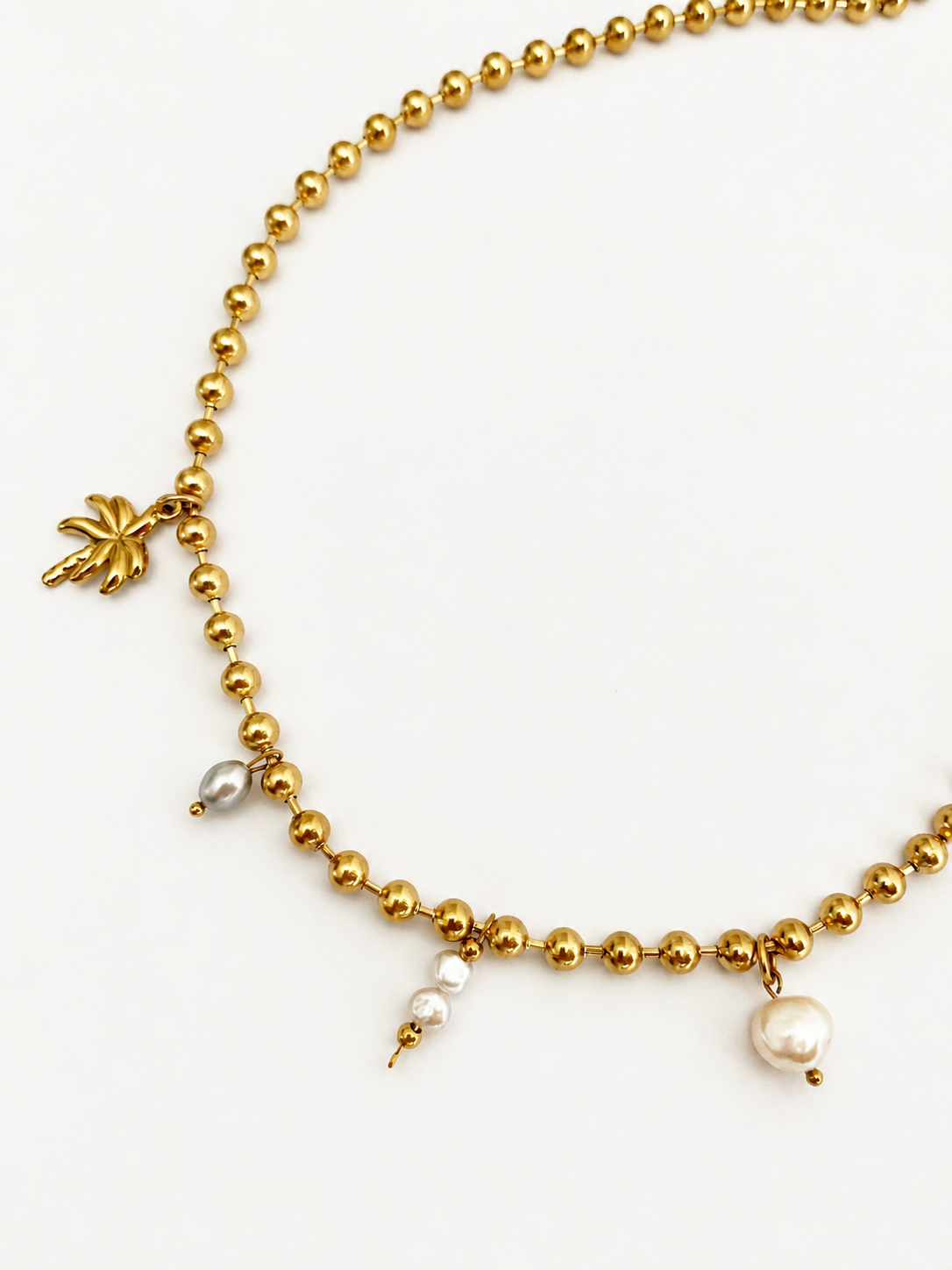 Close-up of a gold beaded charm necklace with white Keshi pearls, a grey oval freshwater pearl and palm tree charm.