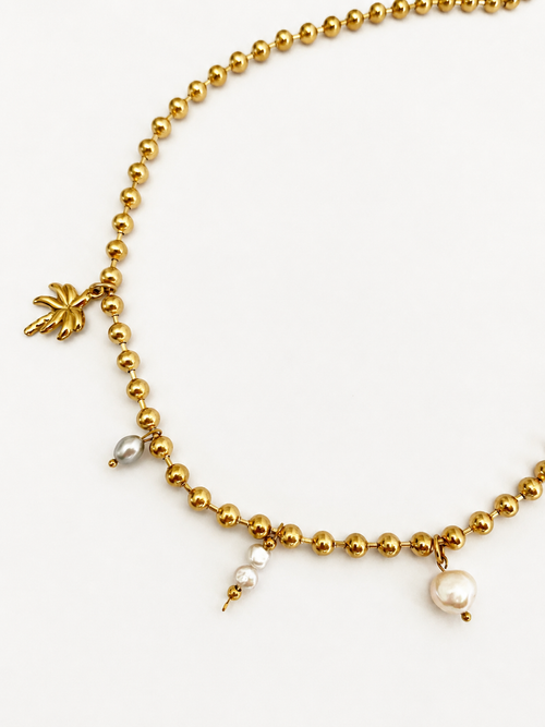 Close-up of a gold beaded charm necklace with white Keshi pearls, a grey oval freshwater pearl and palm tree charm.