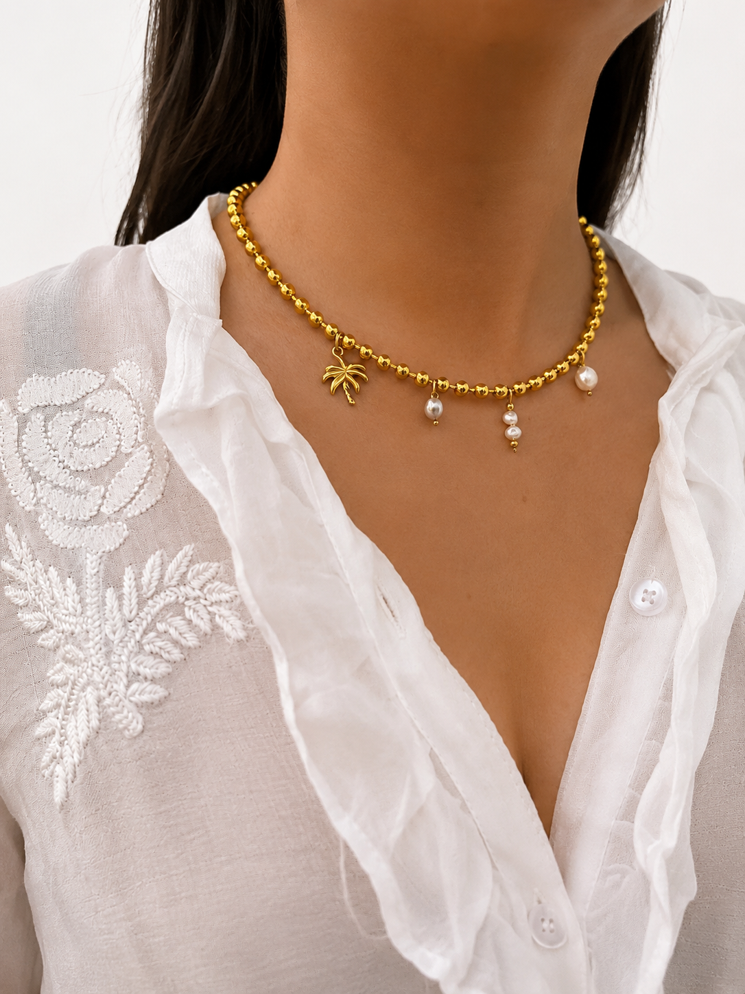 Woman wearing a gold beaded necklace with white Keshi pearls, grey freshwater pearl and palm tree charm