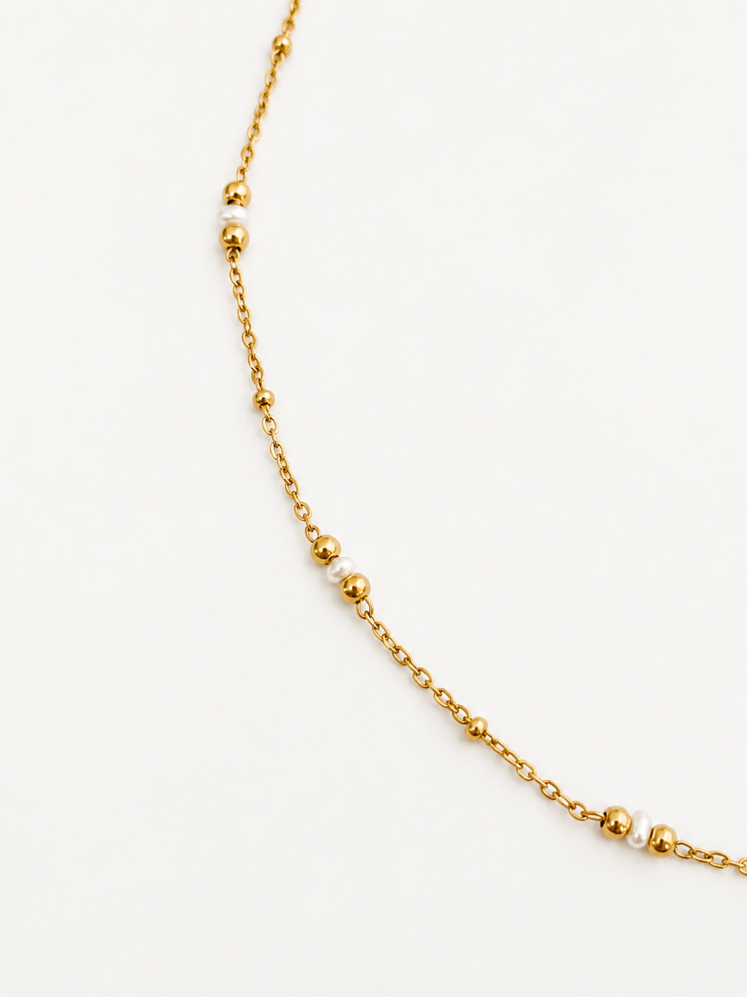 Close-up of a delicate gold chain necklace with petite white Keshi freshwater pearls and polished gold beads
