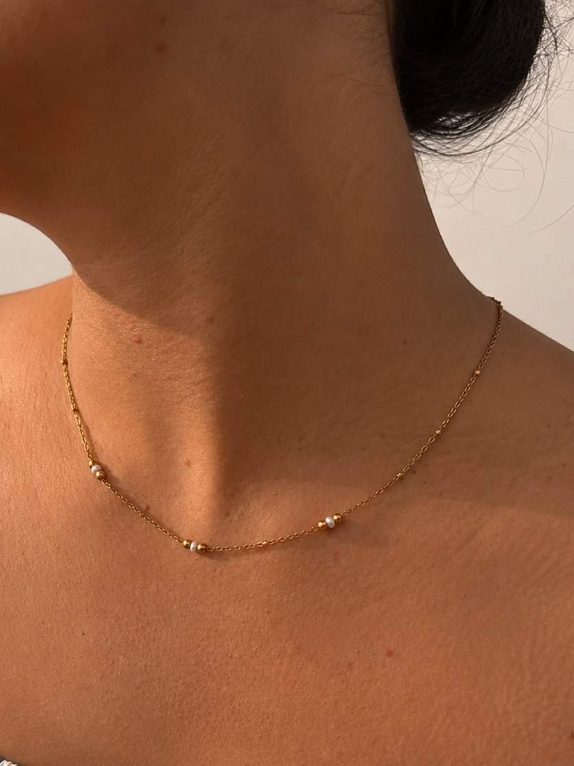 Woman wearing a delicate gold necklace with 2 mm white Keshi cultured freshwater pearls and gold bead accents
