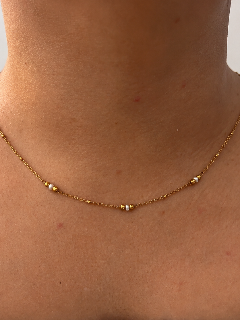 Front view of a delicate gold necklace with 2 mm white Keshi freshwater pearls spaced along the chain