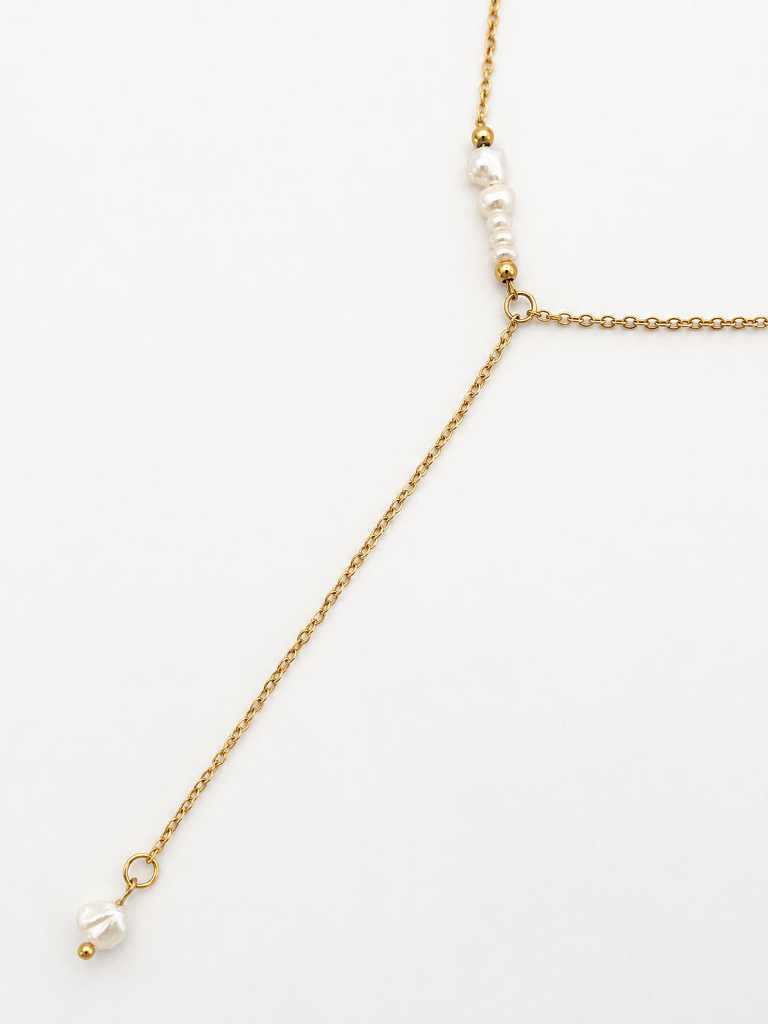 Close-up of a gold lariat necklace with graduated white Keshi freshwater pearls and a pearl drop pendant