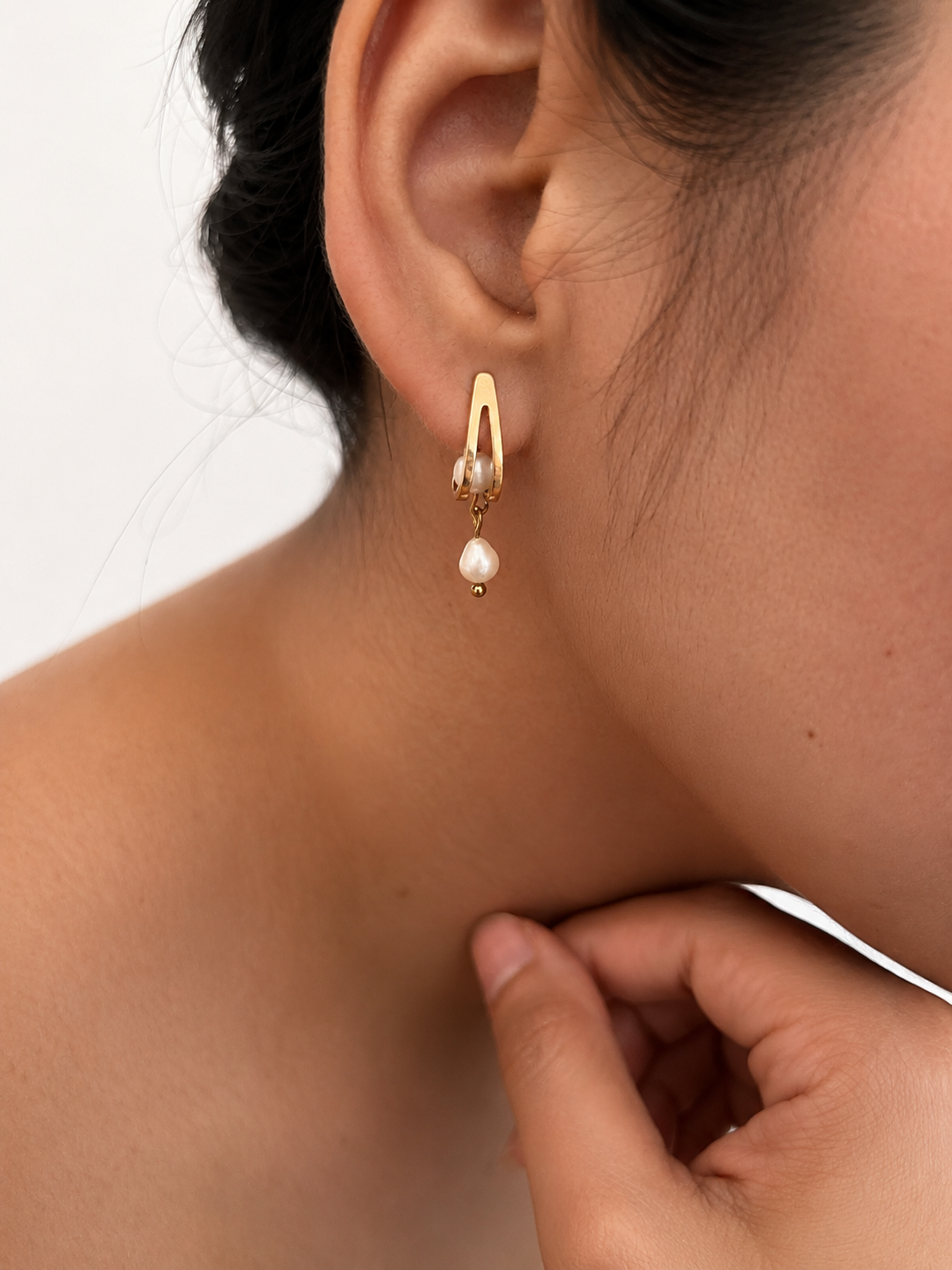 Back and angled view of gold huggie earrings with oval and baroque white freshwater pearls and stud posts.