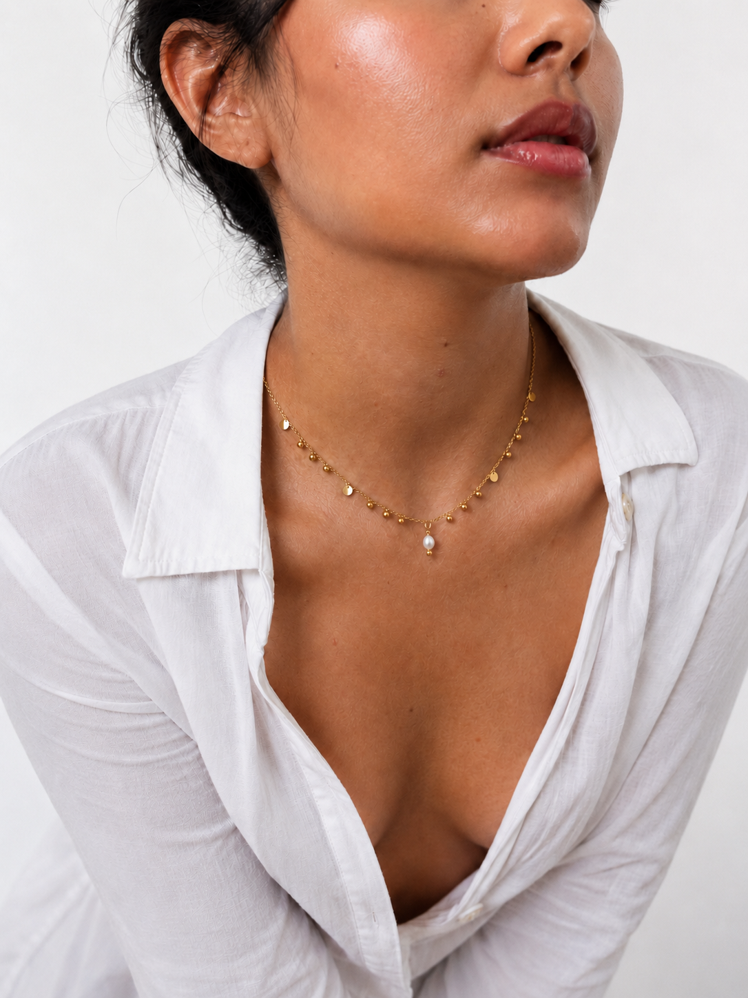 Woman wearing a gold bead charms necklace with an oval white freshwater pearl and polished gold accents