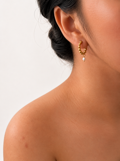 Woman wearing a beaded gold huggie earring with a 6 mm oval white freshwater pearl drop