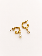 Angled view of beaded gold huggie earrings with 6 mm oval white freshwater pearl drops