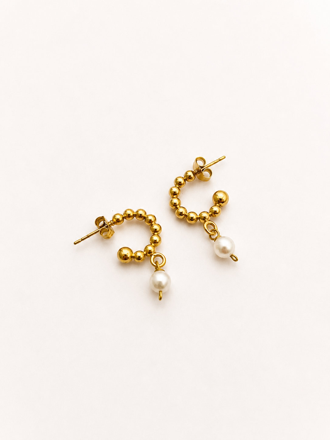 Angled view of beaded gold huggie earrings with 6 mm oval white freshwater pearl drops