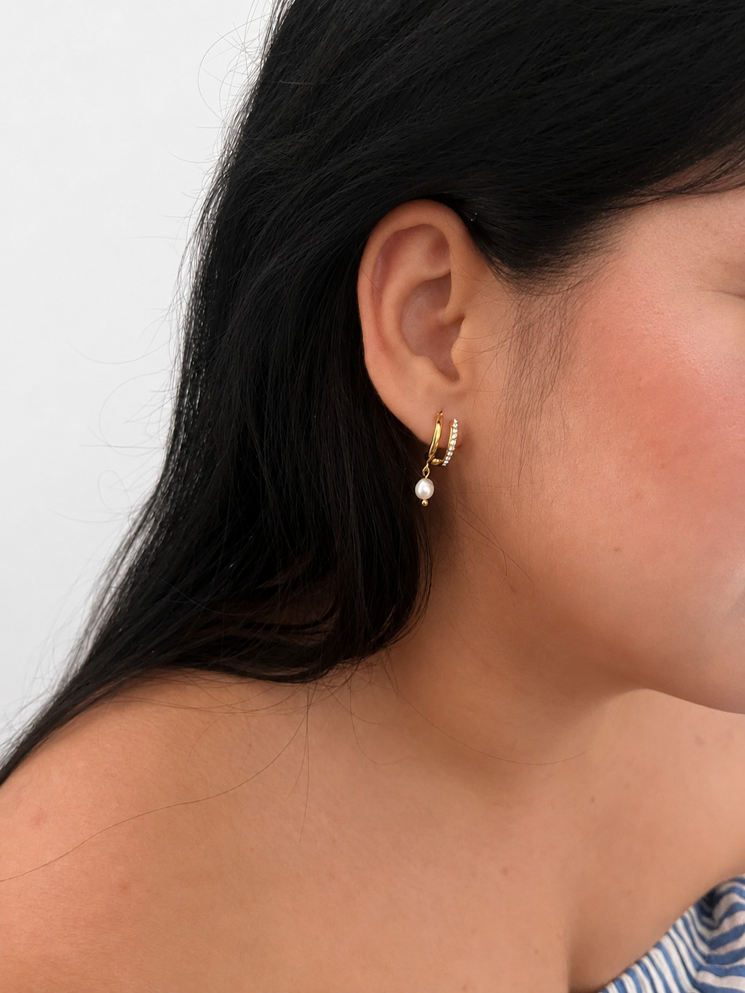 Close-up of a gold half moon huggie earring with a white freshwater pearl and cubic zirconia worn on the ear.