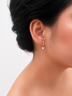Close-up of a gold mini drop earring with a 6 mm oval white freshwater pearl and cubic zirconia worn on the ear.