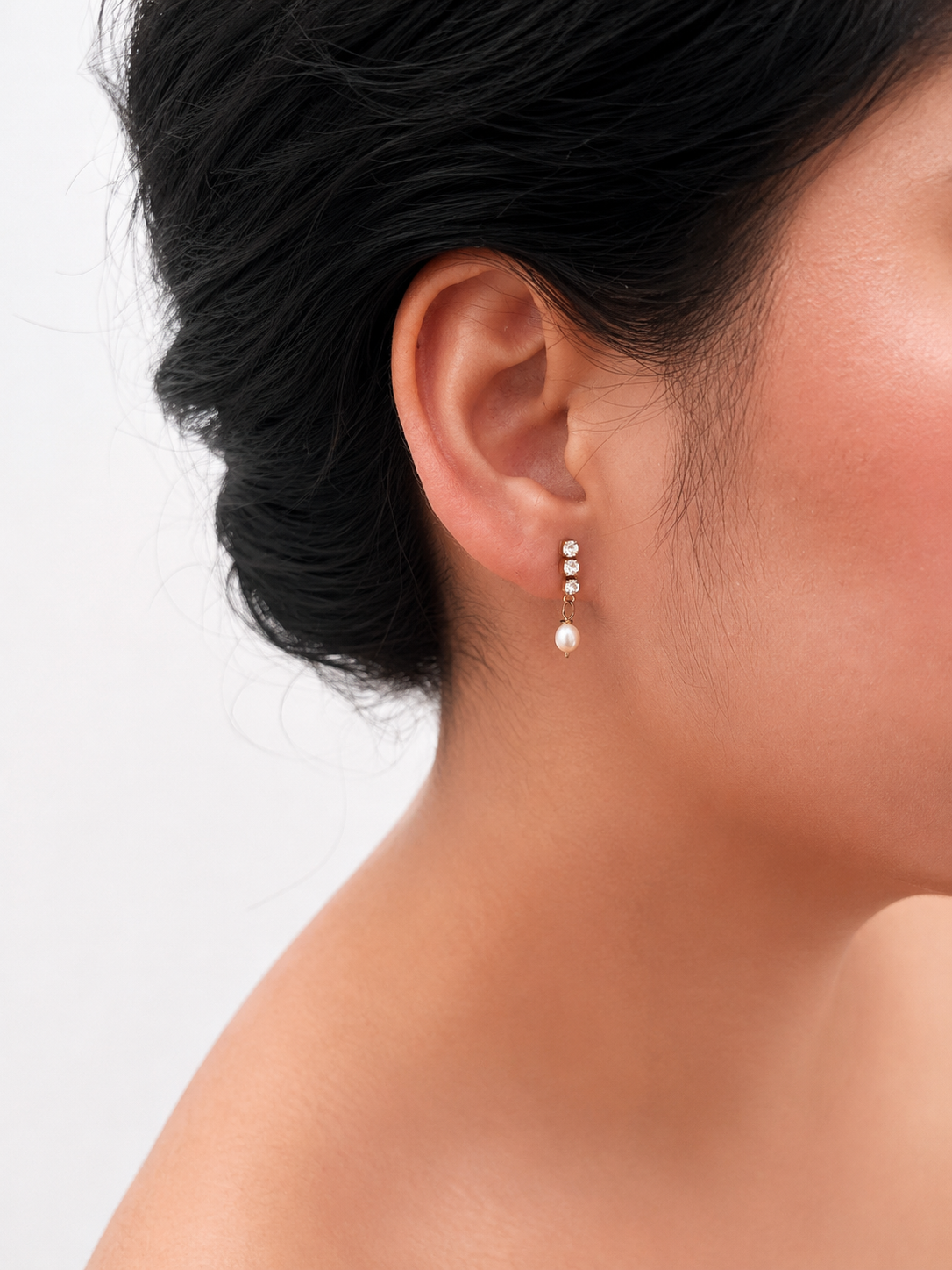 Close-up of a gold mini drop earring with a 6 mm oval white freshwater pearl and cubic zirconia worn on the ear.