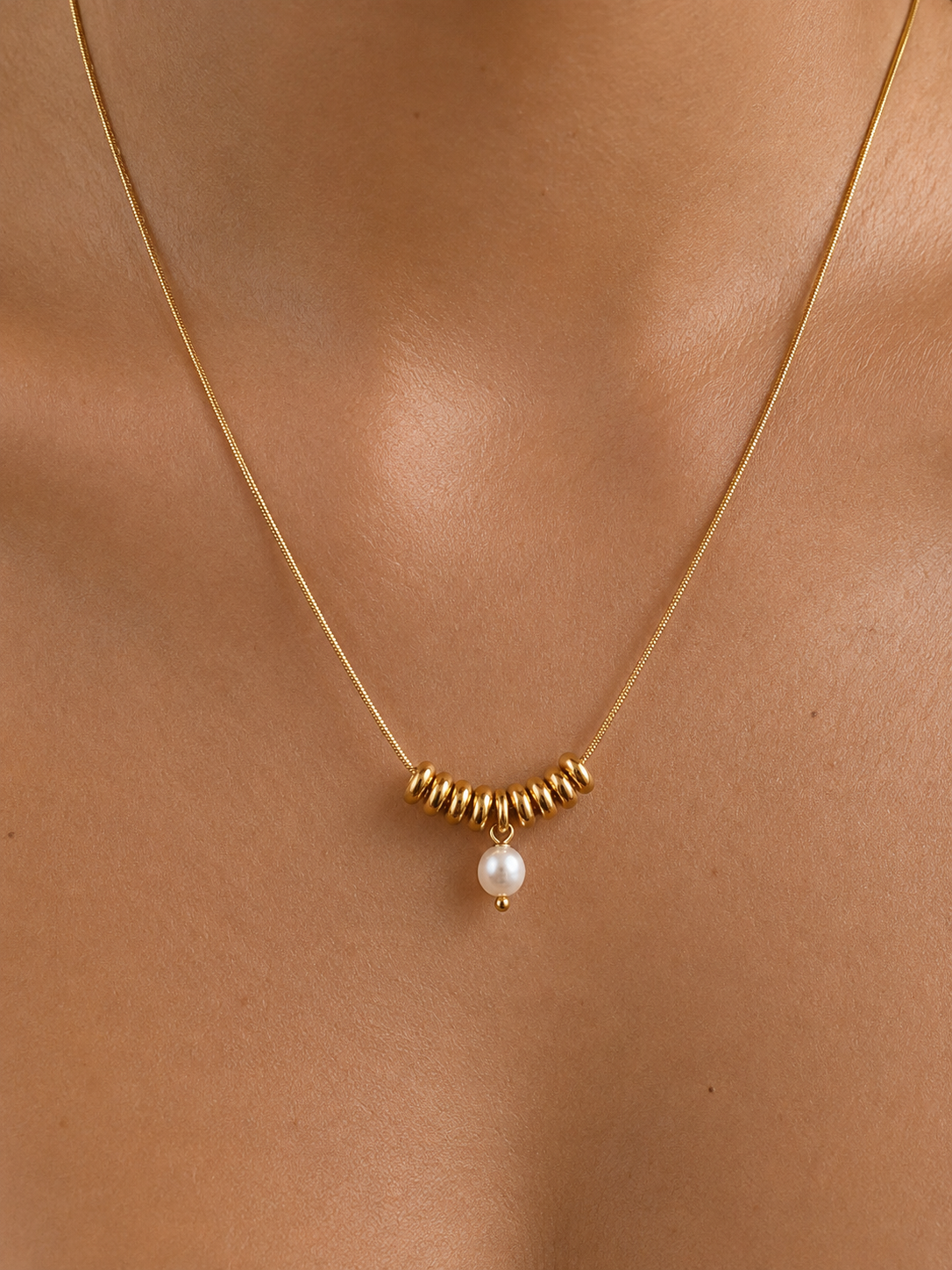 Close-up of a gold Ripple necklace with a 5 mm oval white freshwater pearl worn on the neck.