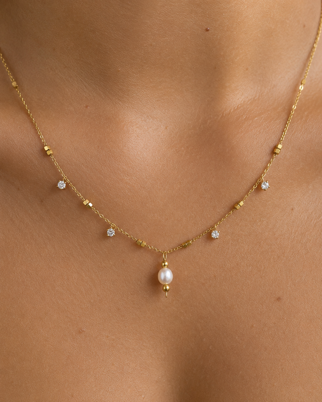 Close-up of a gold necklace with a 5 mm oval white freshwater pearl and cubic zirconia accents worn on the neck