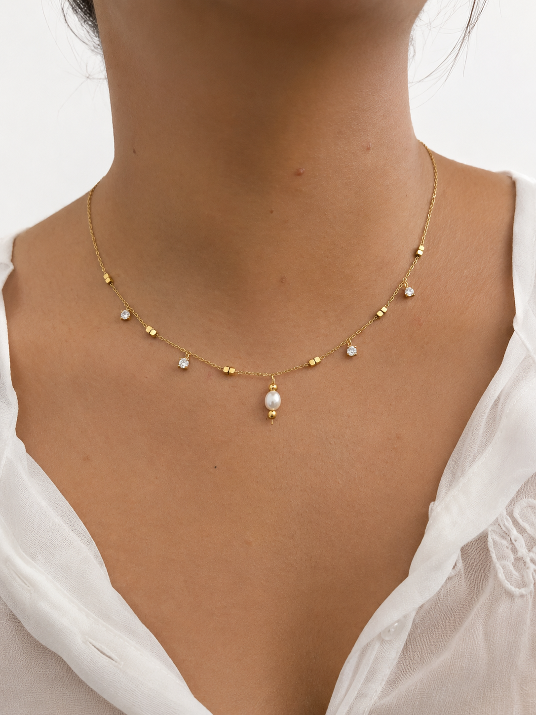 Woman wearing a gold necklace with a 5 mm oval white freshwater pearl and sparkling cubic zirconia accents.