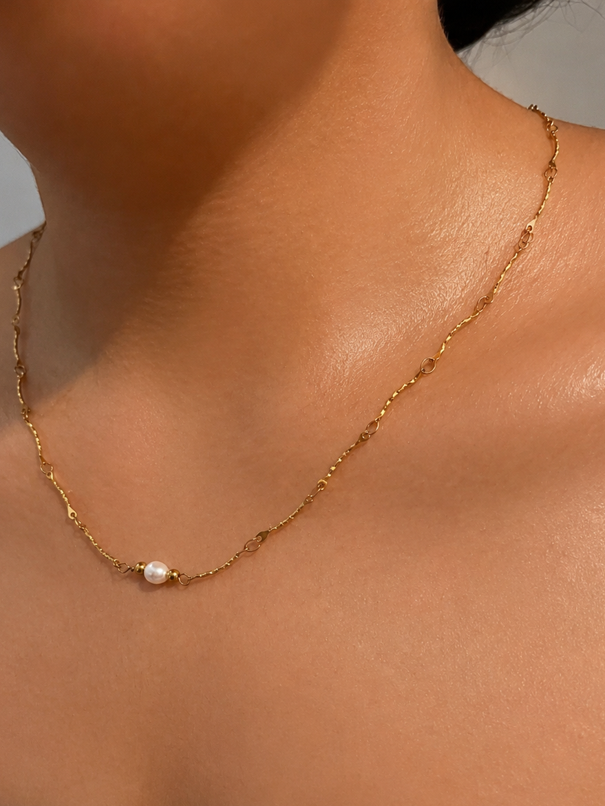 Close-up of a gold Waves necklace with a 6 mm oval white freshwater pearl worn on the neck