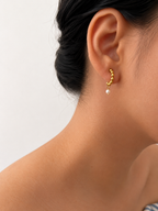 Close-up of a beaded gold huggie earring with an oval white freshwater pearl worn on the ear