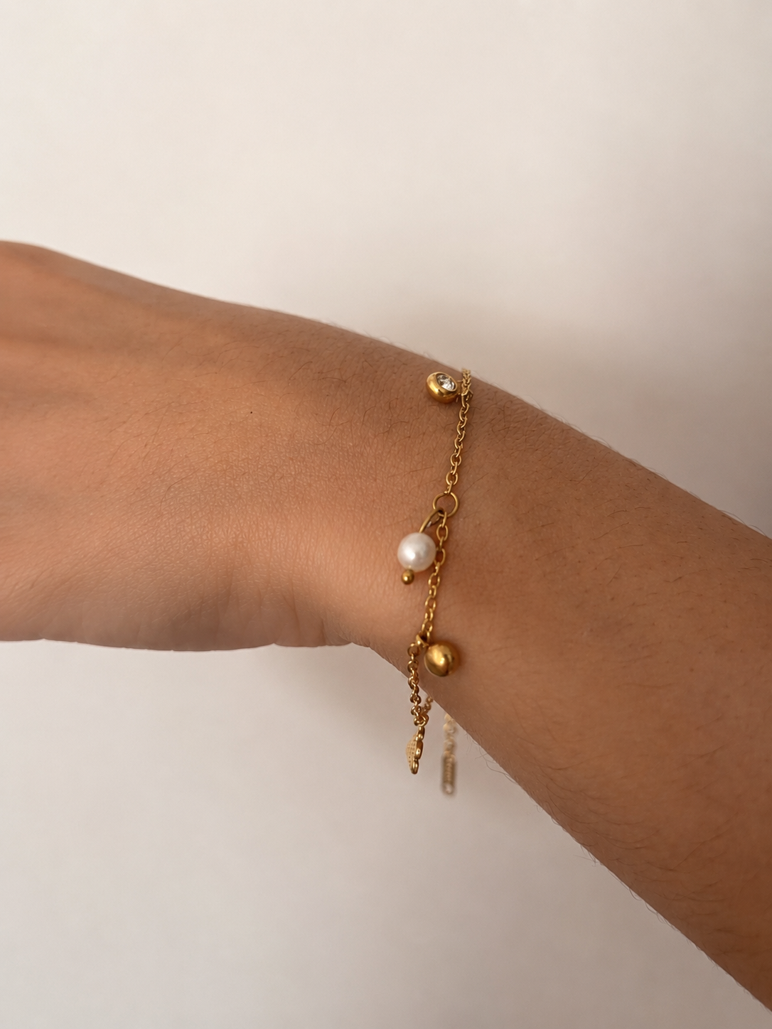 Close-up of a gold chain bracelet with an oval white freshwater pearl, clear stone charms and polished gold details