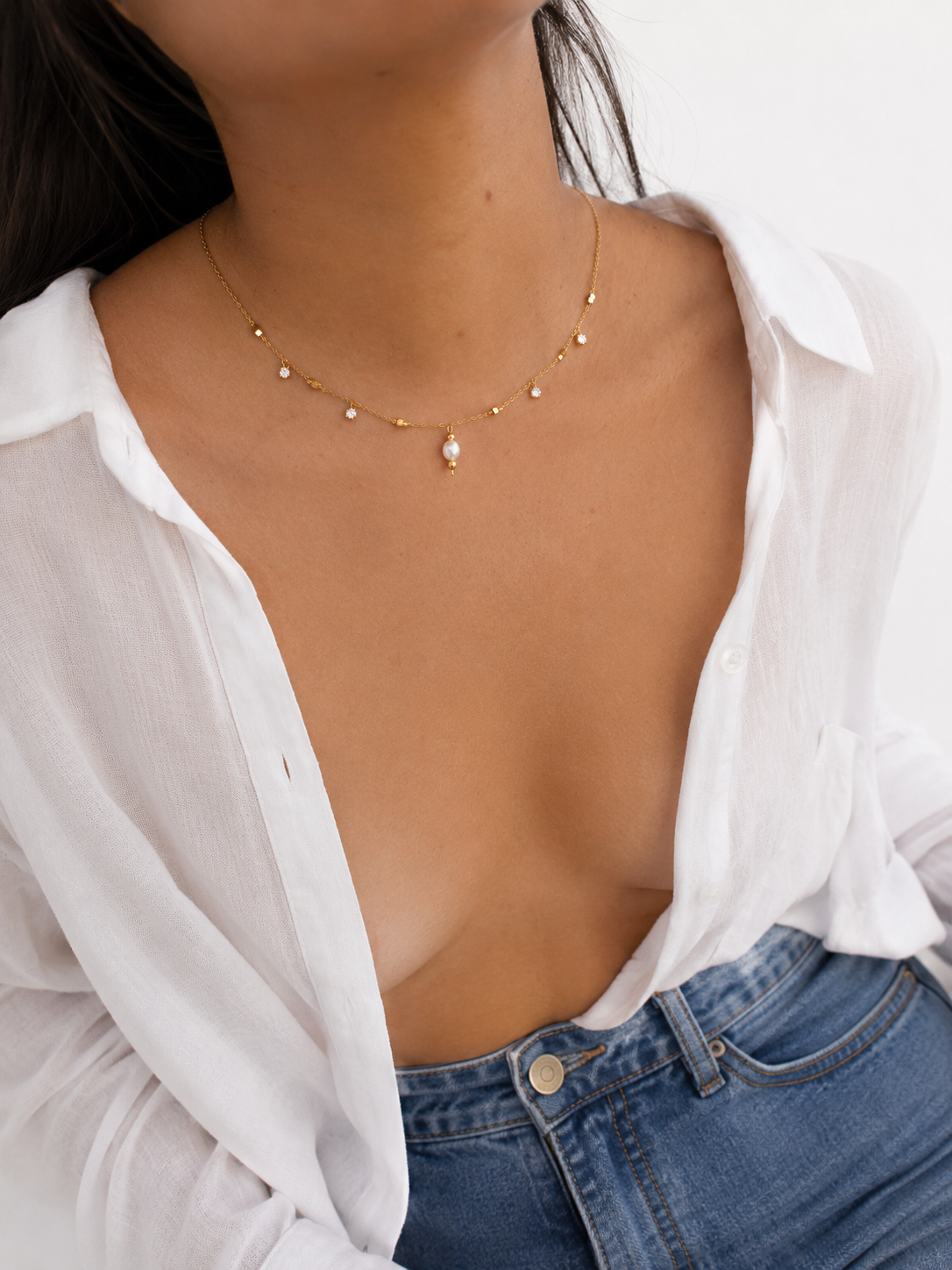 Lifestyle view of a gold necklace with a white freshwater pearl pendant and cubic zirconia accents.