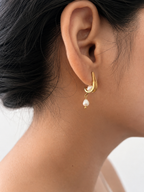 Side view of a gold huggie earring with oval and baroque white freshwater pearls worn on the ear