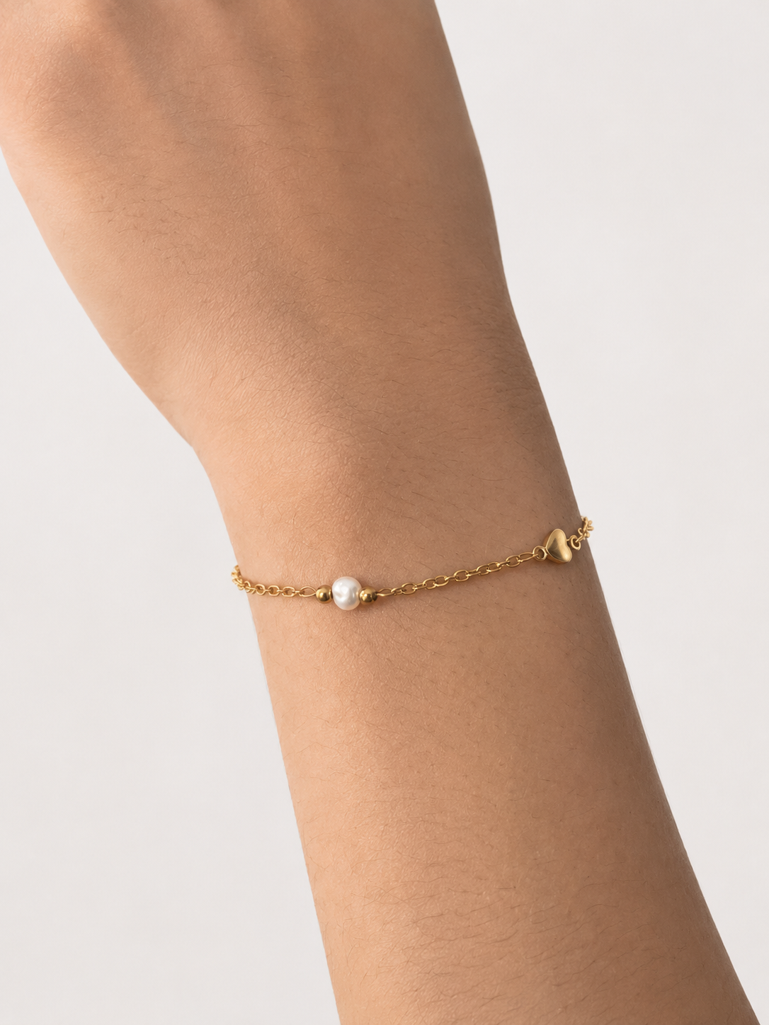 Close-up of a gold chain bracelet with a central white pearl, two gold beads and a small heart charm