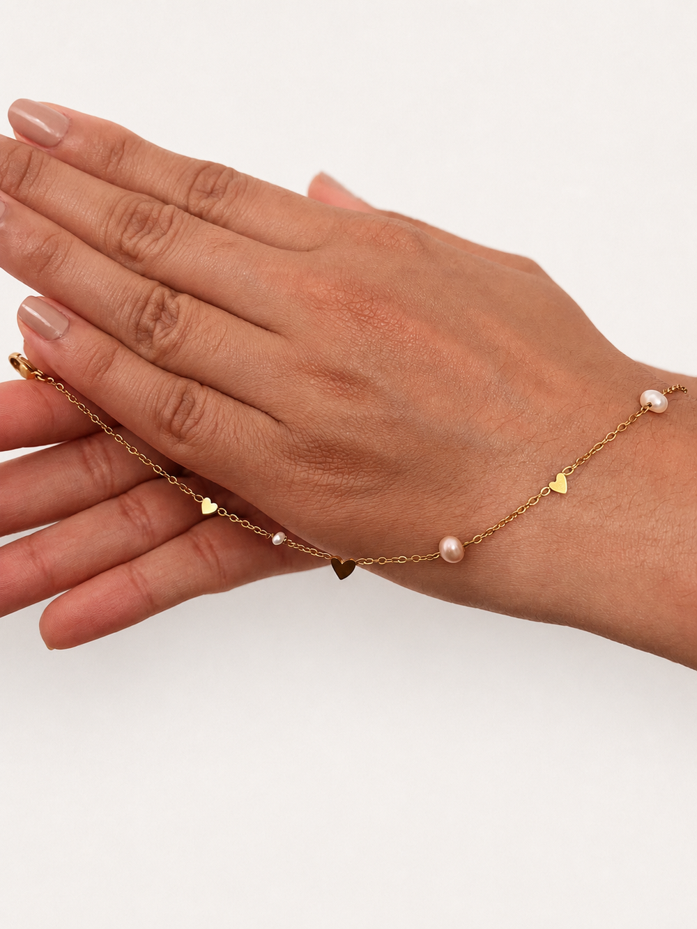 Gold chain bracelet displayed across the hand with white freshwater pearls and polished heart accents
