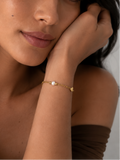 Woman wearing a delicate gold bracelet with a white pearl, polished beads and a petite heart charm