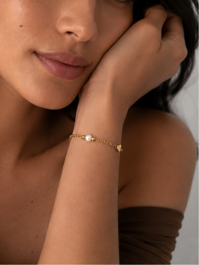 Woman wearing a delicate gold bracelet with a white pearl, polished beads and a petite heart charm