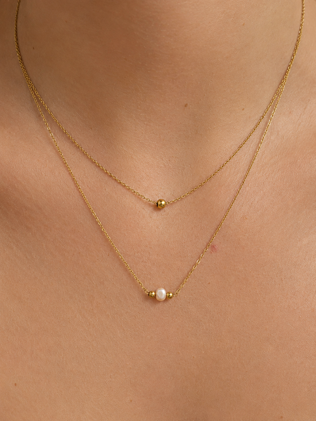 Close-up of a gold layered necklace with a white baroque freshwater pearl centered between polished gold beads