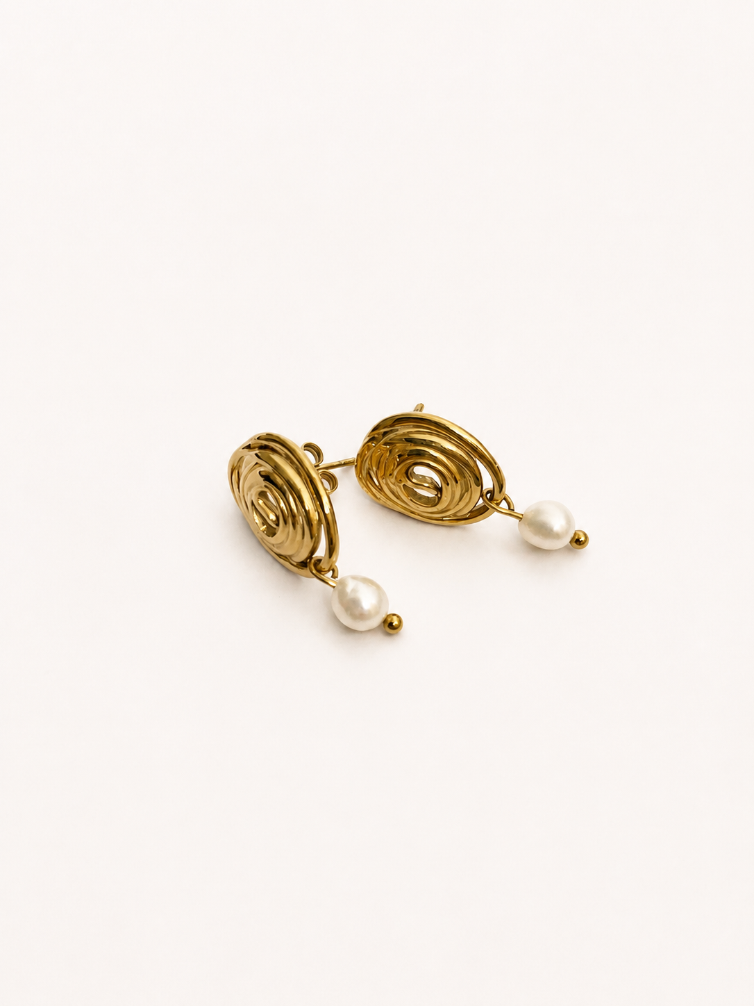 Close-up of gold organic spiral stud earrings with luminous oval white freshwater pearl drops.