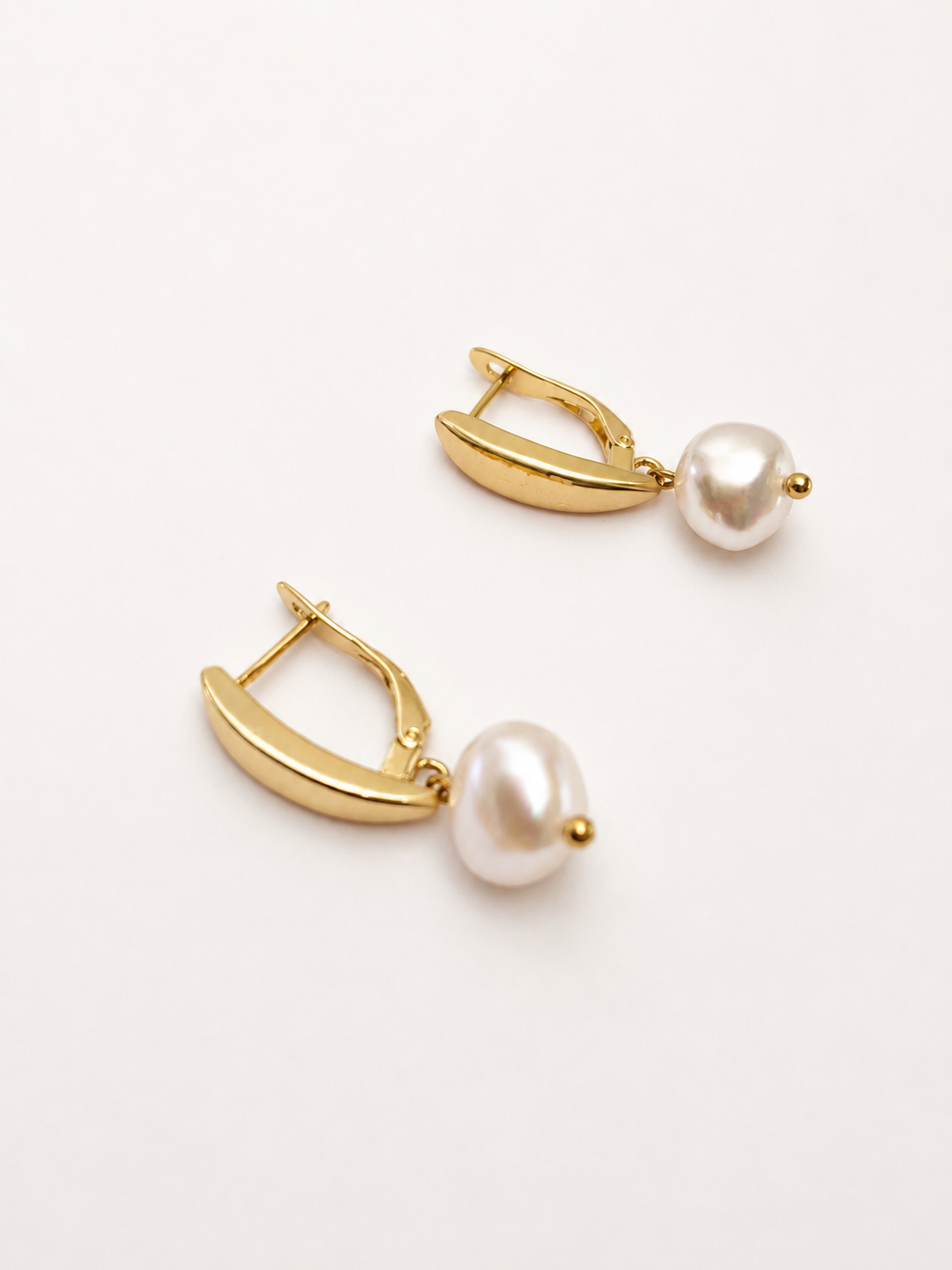 Angled close-up of gold pandan leaf earrings with organic white baroque freshwater pearl drops