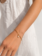 Woman in a white dress wearing a gold paperclip-chain bracelet with an oval white pearl pendant